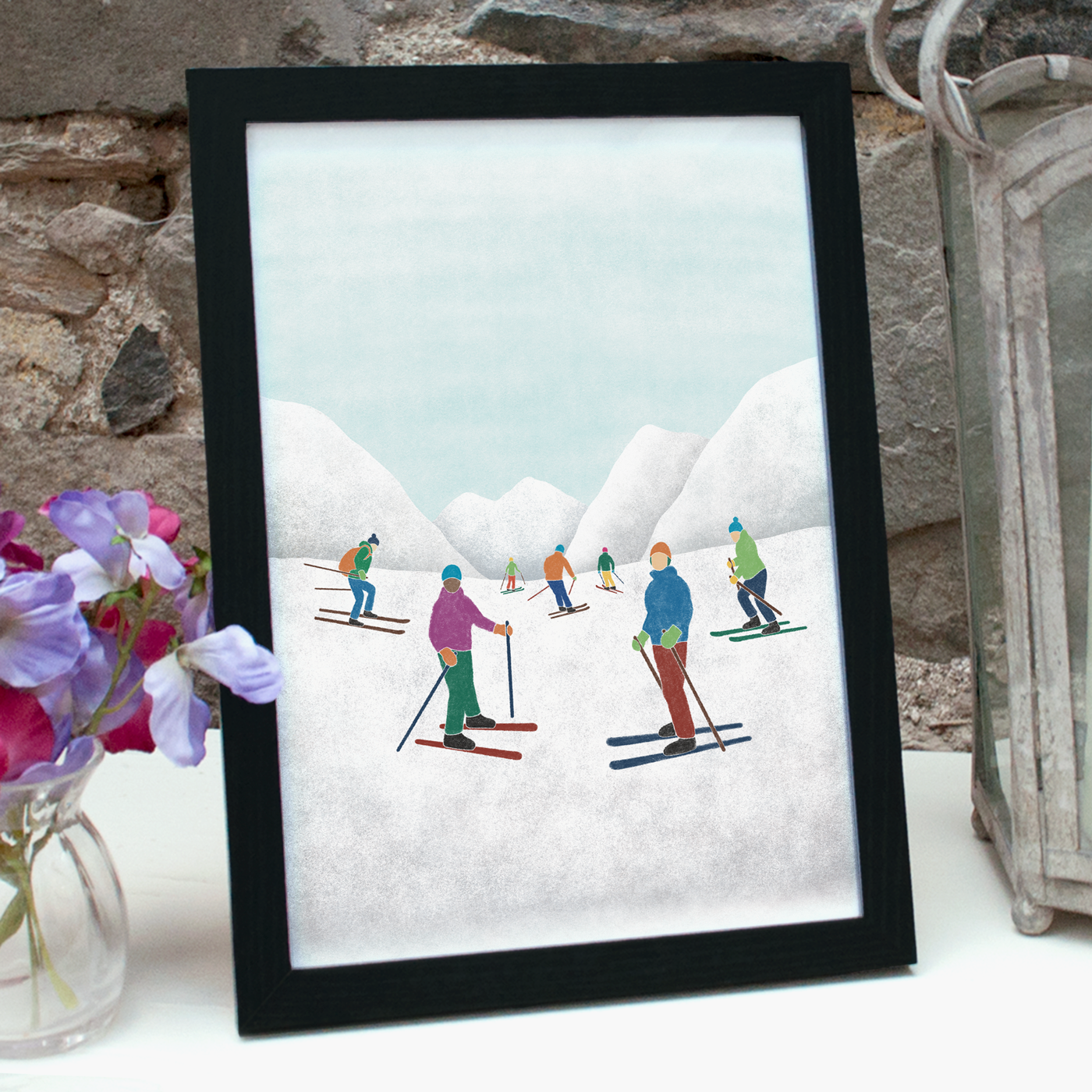 Print of an illustration of 7 skiers in some snowy mountains in a black frame, standing on a table