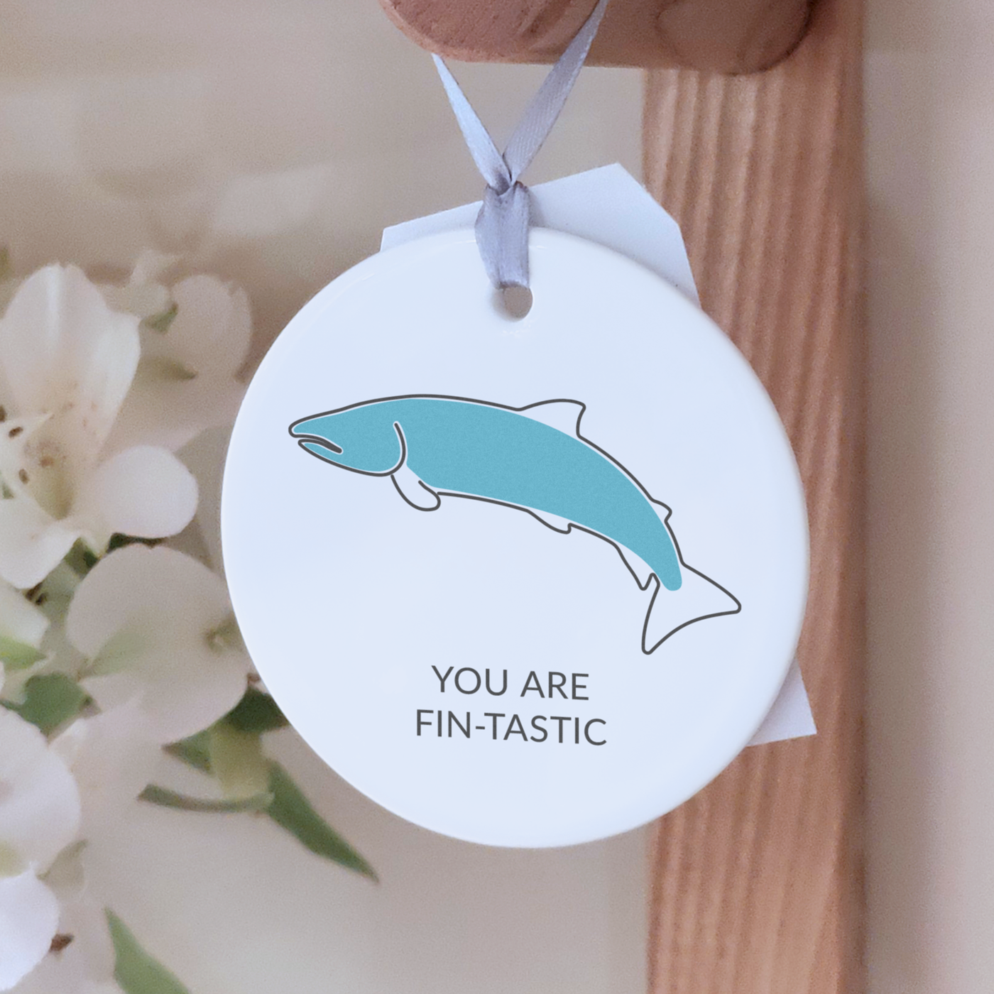Circular ceramic decoration with the message "you are fin-tastic" and an illustration of a fish, hanging from a wooden peg