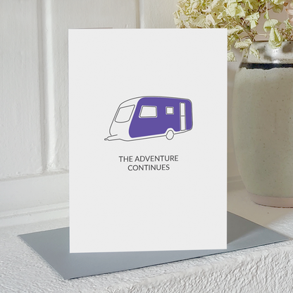 Card with illustration of a caravan and the message the adventure continues, standing on a white shelf