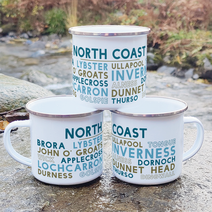Three stacked white enamel mugs with silver rims, standing on a rock in front of foliage and a river. Each mug features the words "North Coast" in blue, with the names of various towns around the North Coast of Scotland underneath