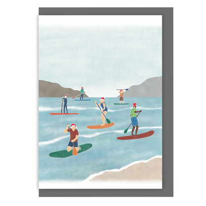 Paddle boarding Christmas card with an illustration of a group of paddle boarders wearing Santa hats while out on the water, on a white background