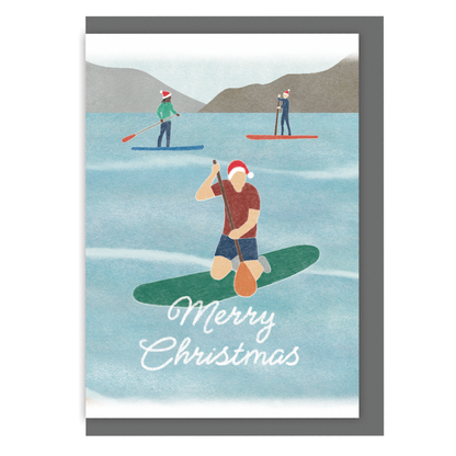 Paddle boarding Christmas card with three paddleboarders wearing Santa hats and the message "Merry Christmas" on a white background