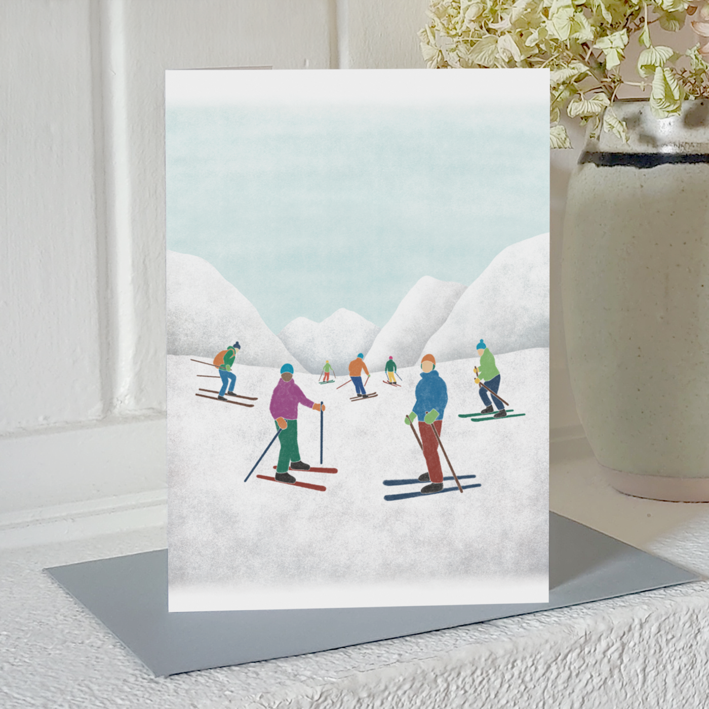 Greetings card with an illustration of skiers and snowy mountains, standing on a mantelpiece