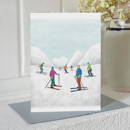 Greetings card with an illustration of skiers and snowy mountains, standing on a mantelpiece