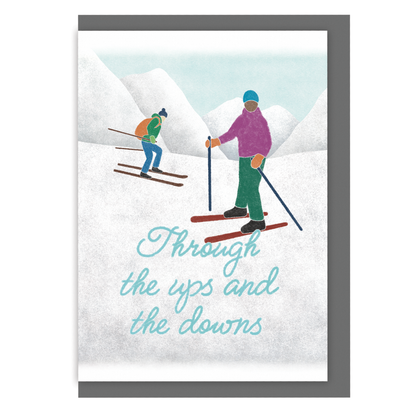 Greetings card with skiers on a snowy mountain and the text 'Through the ups and the downs', on a white background
