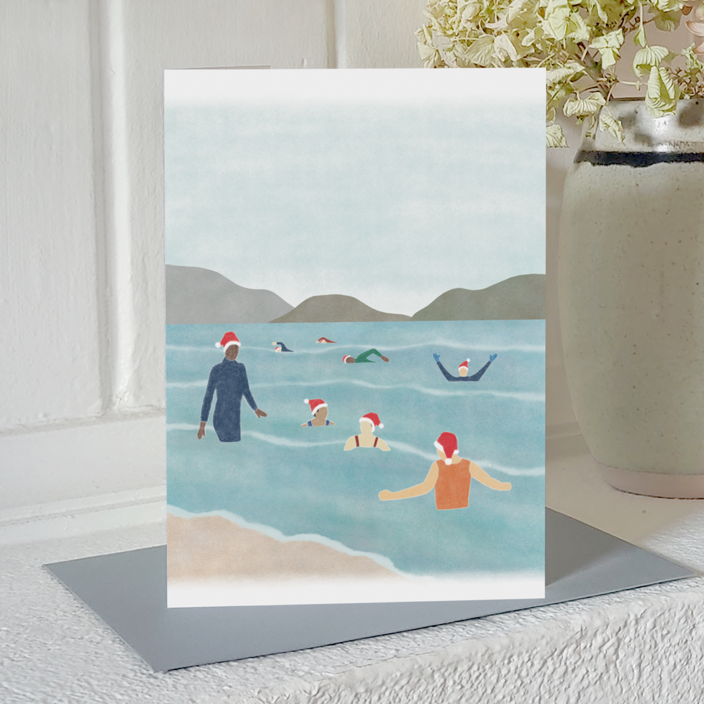 Wild swimming Christmas card with an illustration of a group of cold water swimmers wearing Santa hats, standing on a mantelpiece