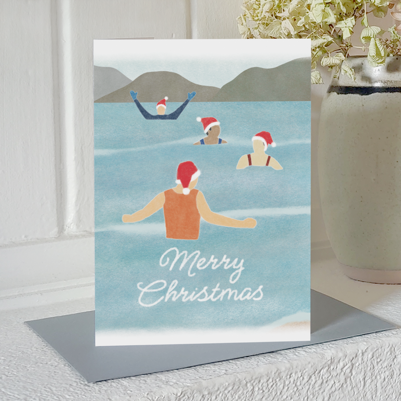Wild swimming Christmas card with four festive swimmers and the text "Merry Christmas", standing on a mantelpiece
